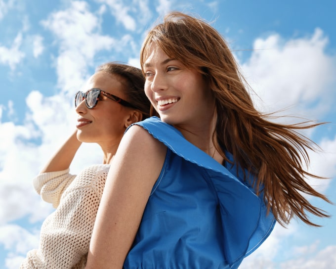 Two women back to back looking to the left against a backdrop of a blue sky with clouds